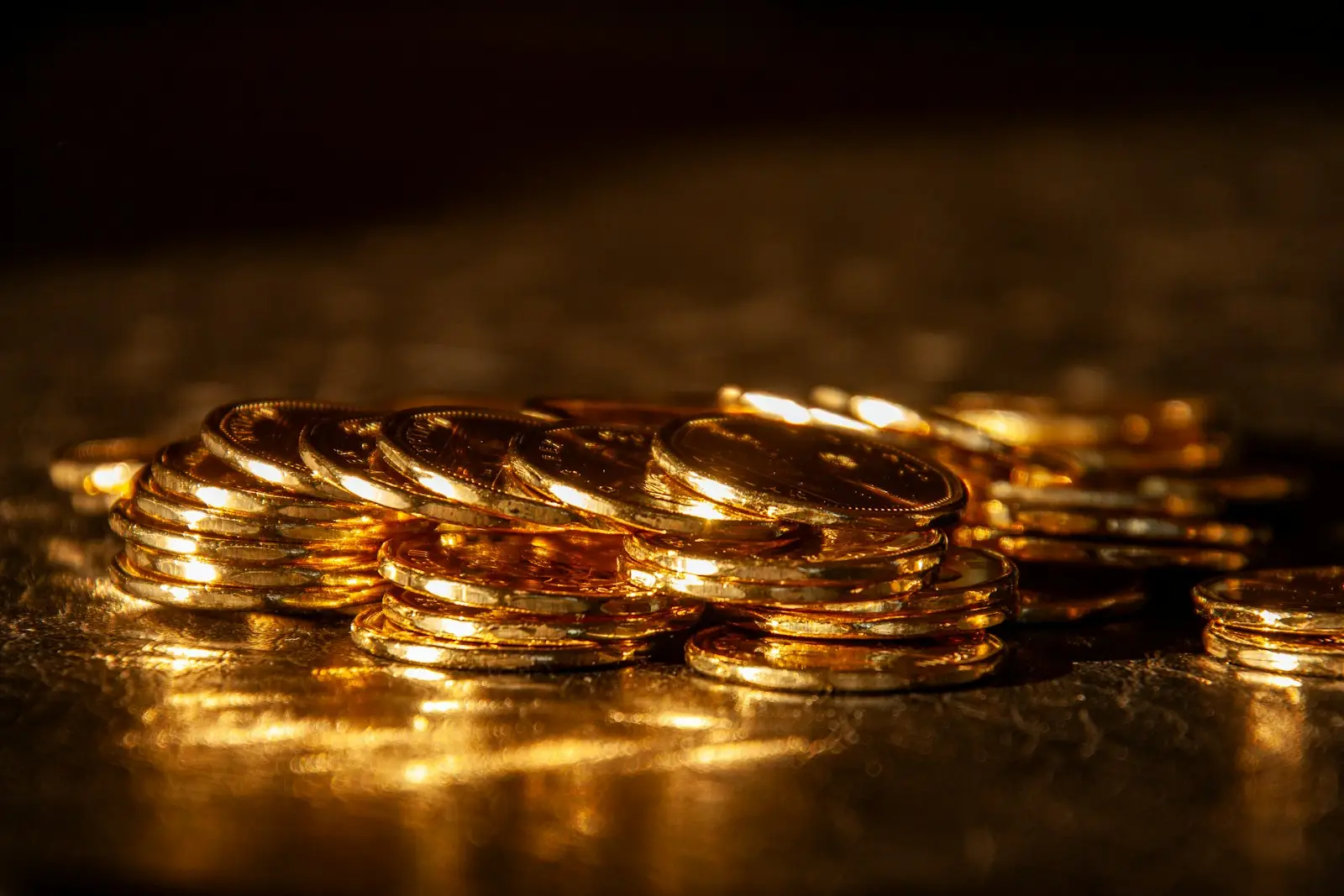 A close-up of stacked gold-coloured Canadian dollar coins lit from the side against a dark background
