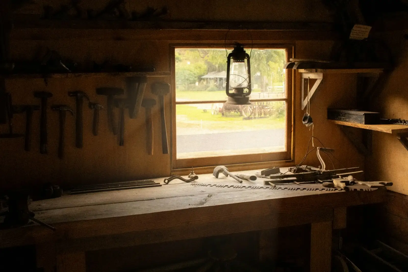 A rustic wooden workbench under a window with hammers hanging on the wall and old hand tools on the bench