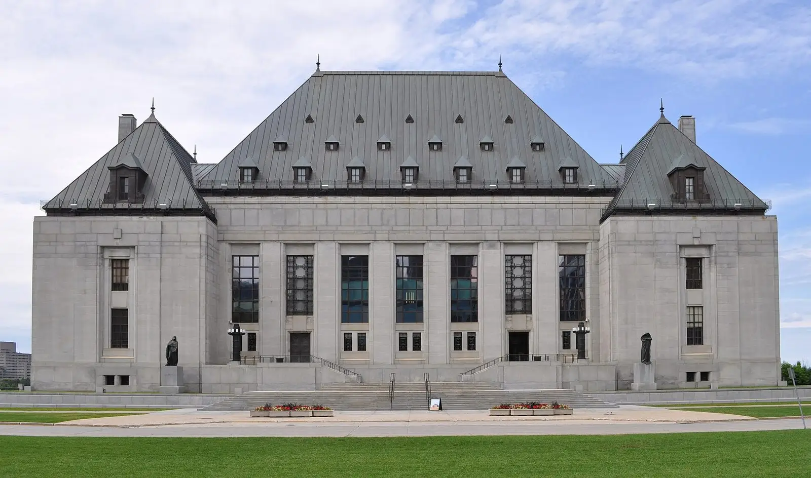The Supreme Court of Canada building in Ottawa, a grey stone building with a steep copper roof, on a summer day